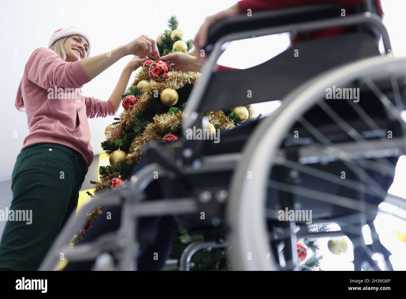 Femme et ami en fauteuil roulant accrochant le ballon de noël rouge sur l'arbre du nouvel an Banque D'Images