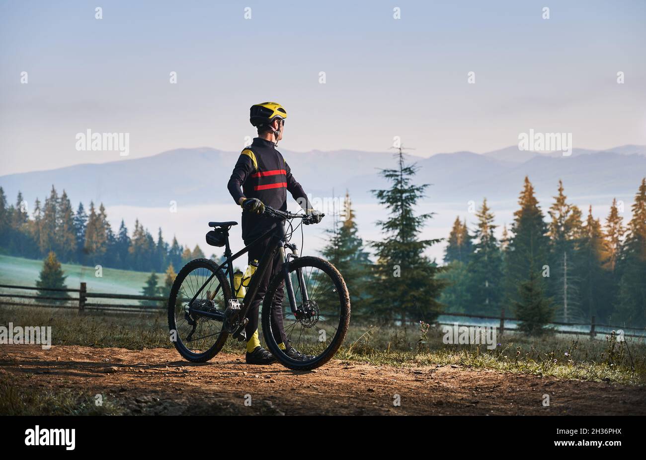 Cycliste masculin debout avec vélo avec des conifères et des collines sur  fond.Homme cycliste appréciant une balade à vélo dans les montagnes le  matin.Concept de sport, de vélo et de loisirs actifs