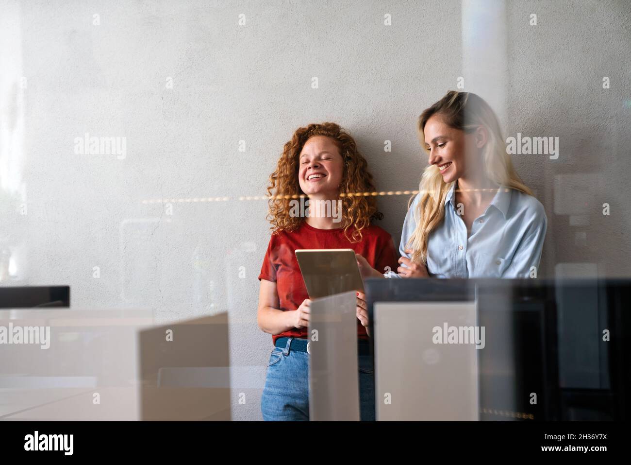 Des femmes d'affaires souriantes travaillant ensemble en ligne sur une tablette au bureau Banque D'Images