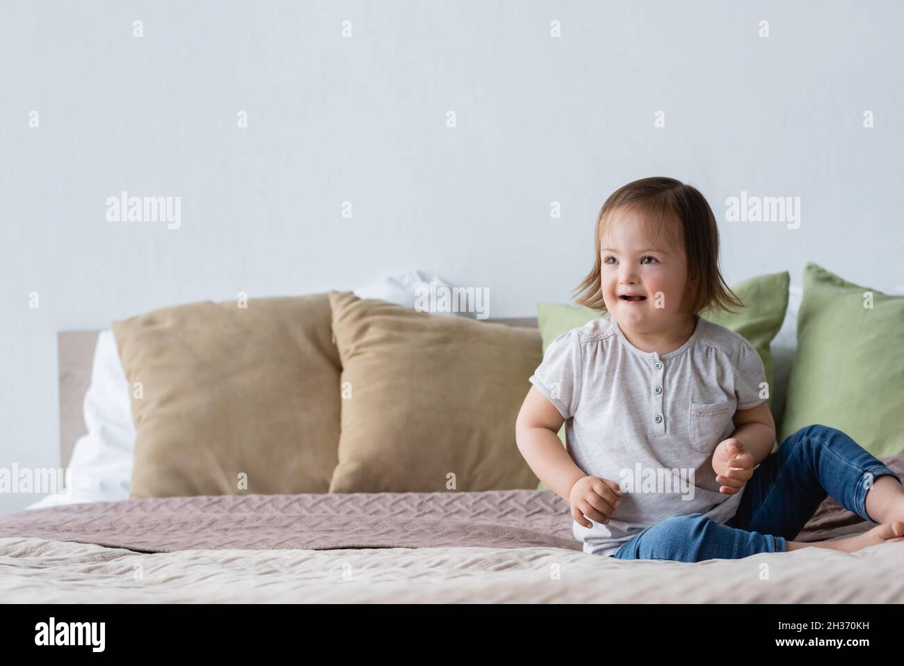 Jeune fille souriante avec syndrome de Down assise sur le lit Banque D'Images