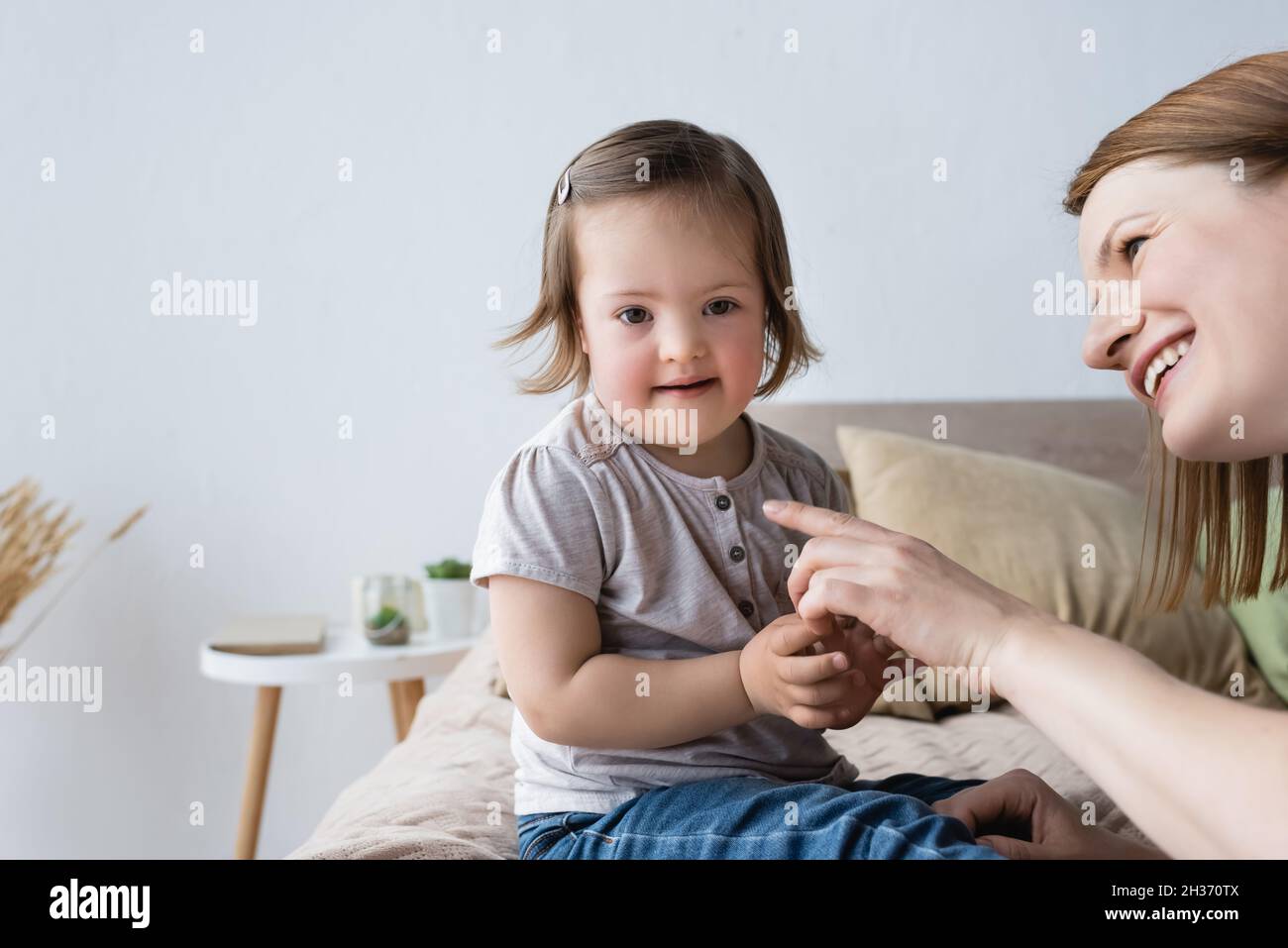 Mère souriante pointant avec le doigt sur la petite fille avec le syndrome de Down dans la chambre Banque D'Images