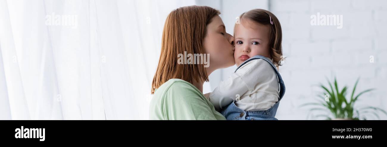 Femme embrassant un enfant tout-petit avec le syndrome de Down à la maison, bannière Banque D'Images