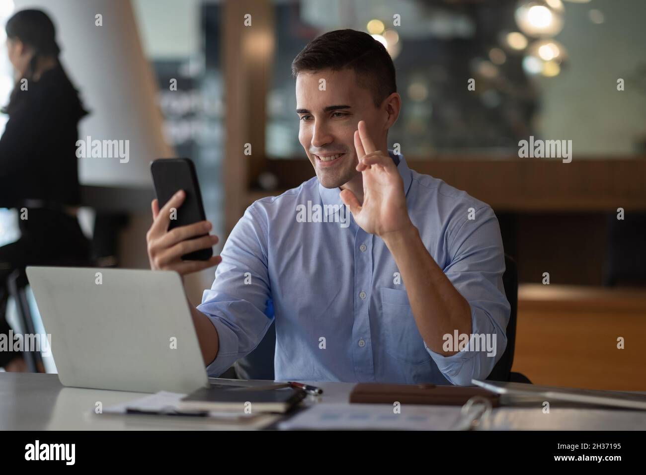 Homme d'affaires joyeux et joyeux utilisant l'application pour smartphone pour la communication virtuelle, tenant le téléphone à la main et en agitant à la webcam, tenant des appels vidéo assis à Banque D'Images