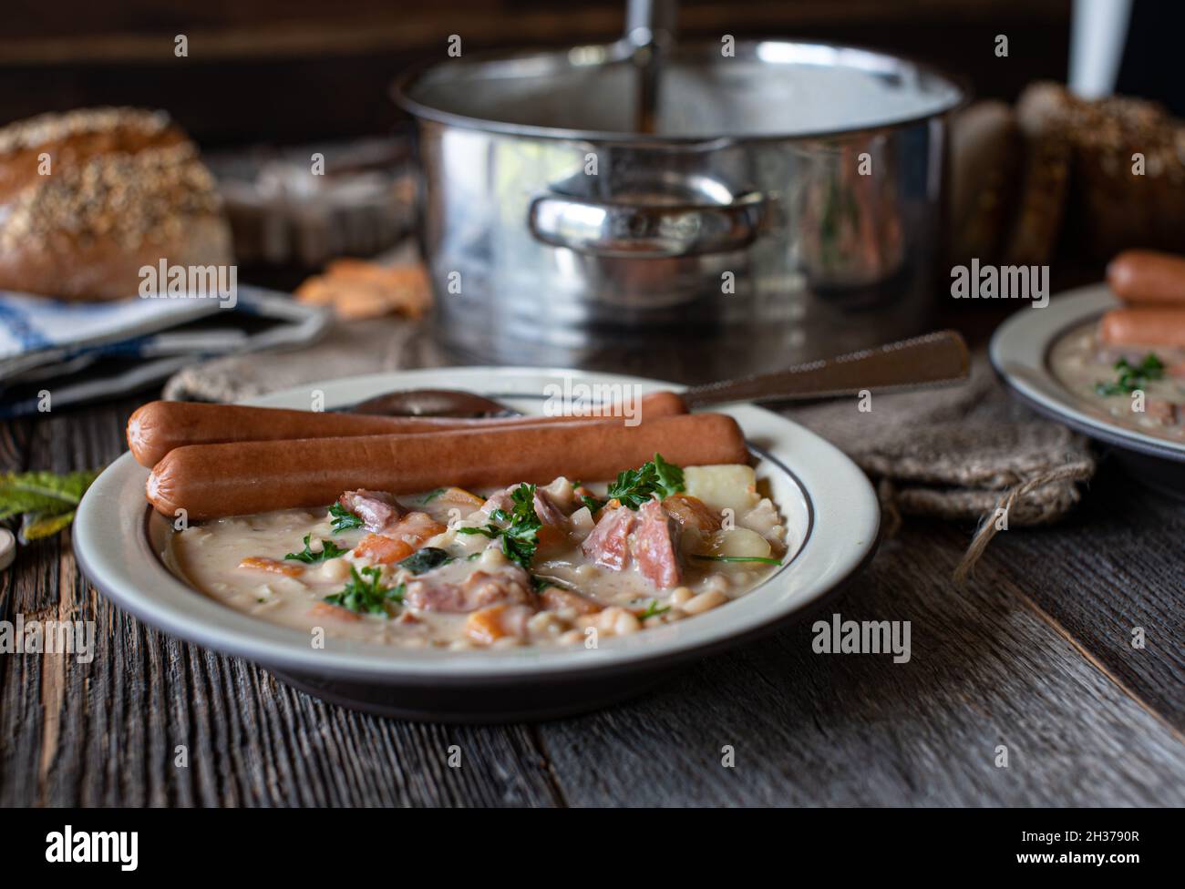 Table rustique pour le dîner ou le déjeuner avec une soupe aux haricots blancs maison et des saucisses de vienne.Servi avec du pain Banque D'Images