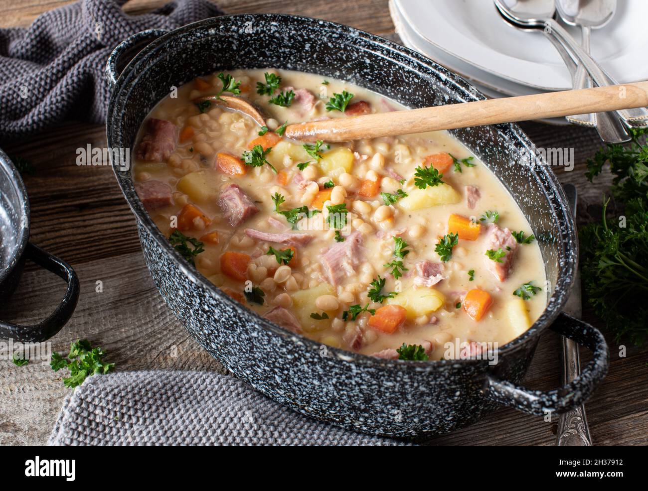 Ragoût rustique avec haricots blancs, viande de porc fumée, légumes-racines et pommes de terre.Servi dans un ragoût sur une table en bois d'en haut Banque D'Images