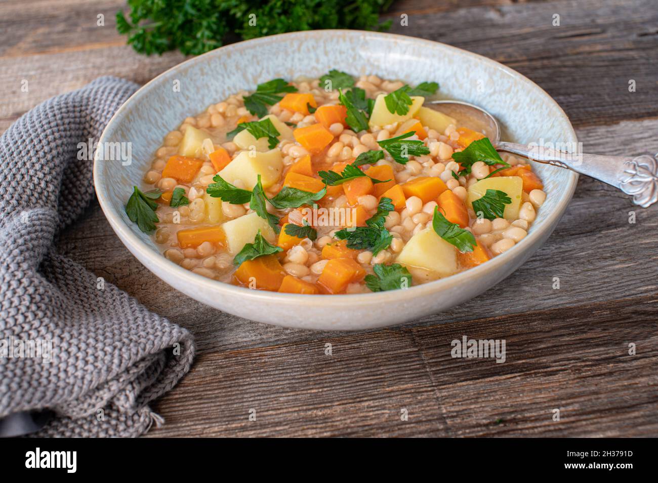 Soupe de haricots blancs vegan avec pommes de terre et légumes-racines isolés sur une table en bois avec une cuillère Banque D'Images