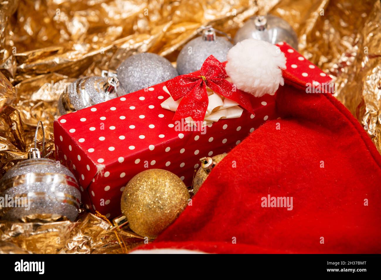 Cadeau de Noël décoré de papier à pois rouges et blancs avec glands rouges et décorations de boules d'arbre de Noël et chapeau rouge du père noël isolé sur un tibia Banque D'Images