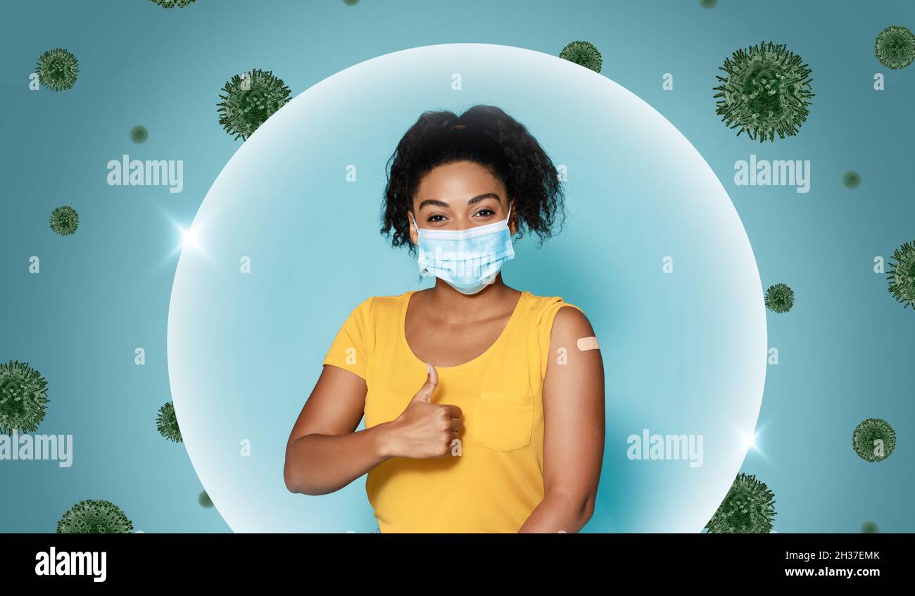 Une jeune femme noire heureuse en masque montre l'épaule avec l'aide de bande après la vaccination et le pouce vers le haut, dans la bulle Banque D'Images