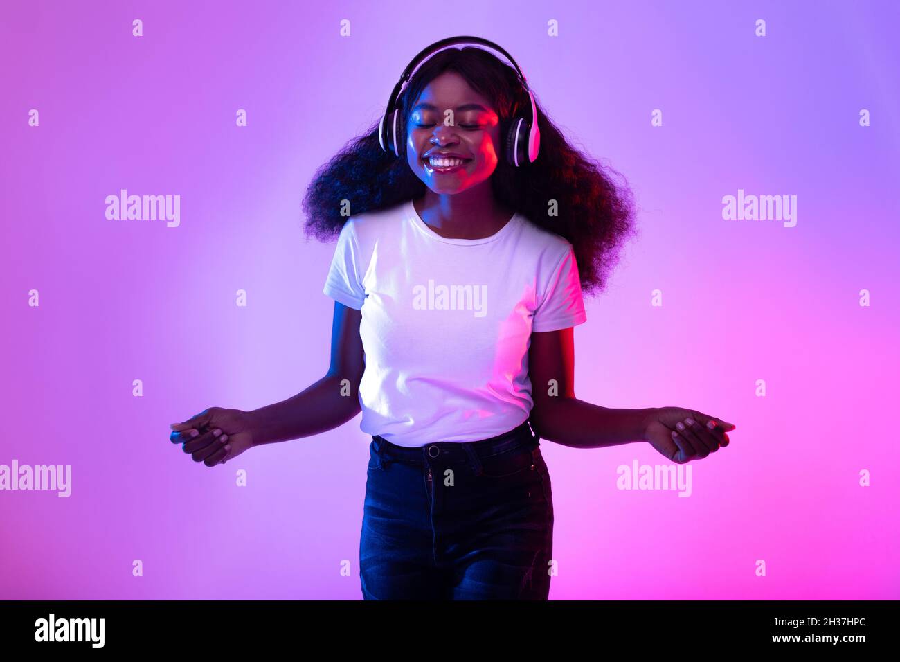 Portrait d'une jeune femme noire gaie, avec casque sans fil, qui écoute de la musique à la lumière du néon Banque D'Images