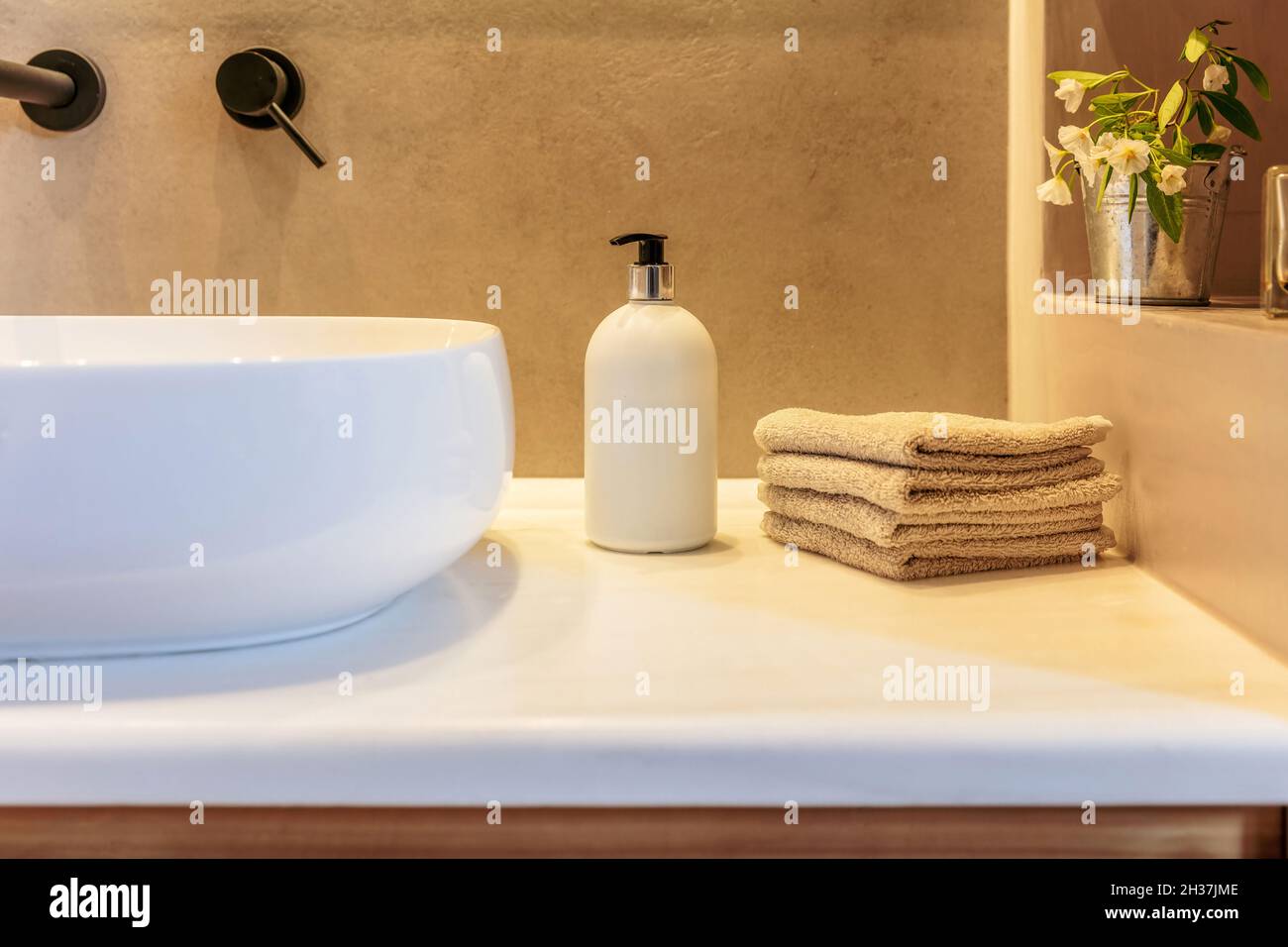 Décoration intérieure moderne dans la salle de bains.Essuie-mains pliés, distributeur de savon et lavabo blanc sur une table en marbre.Robinets noirs et décoration de plantes fraîches.COM Banque D'Images