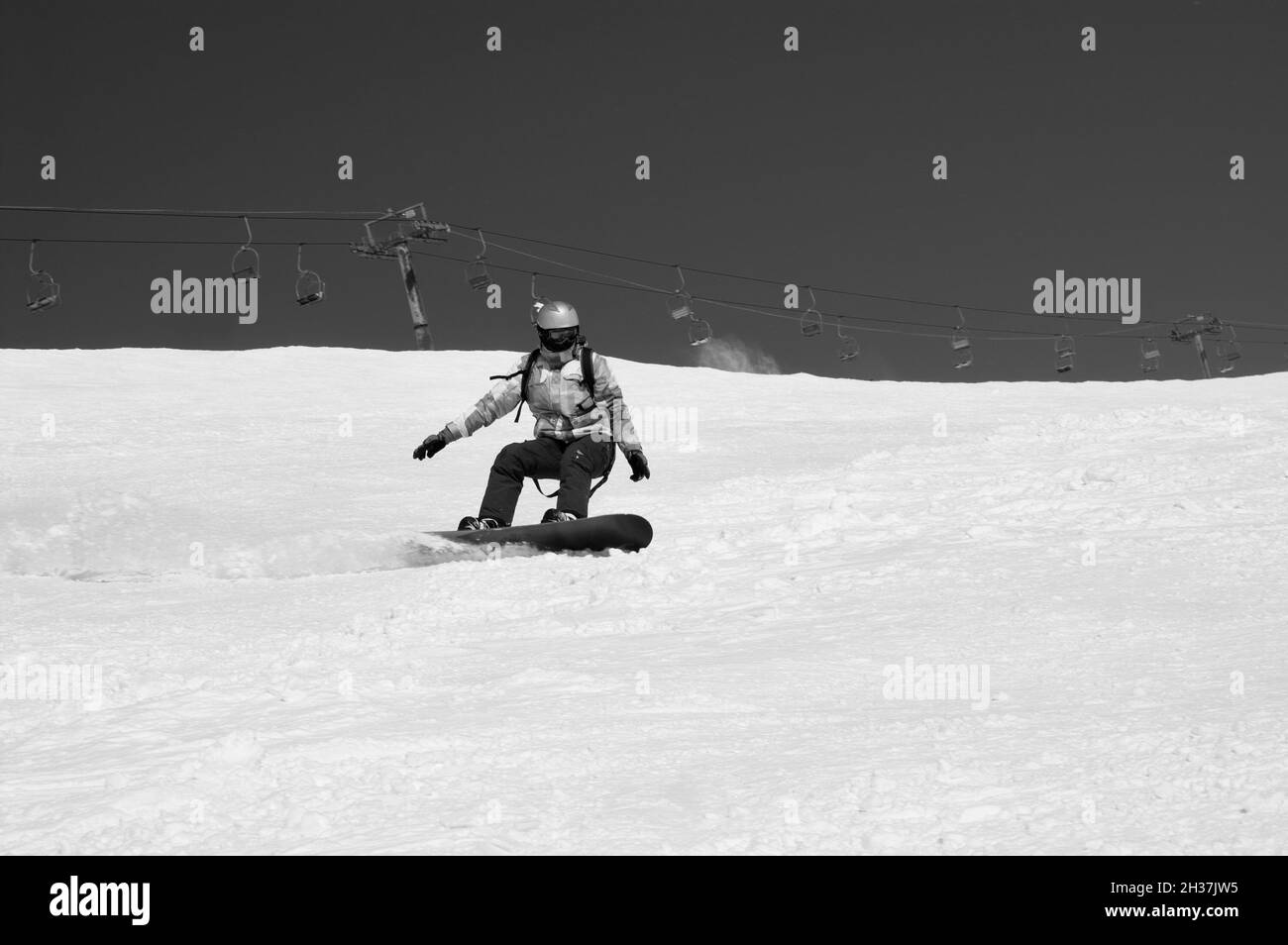La snowboardeuse descend sur une piste de ski enneigée dans les montagnes d'hiver par beau temps.Ancien télésiège en arrière-plan.Caucase montagnes, région Dombay.Noir et blanc Banque D'Images