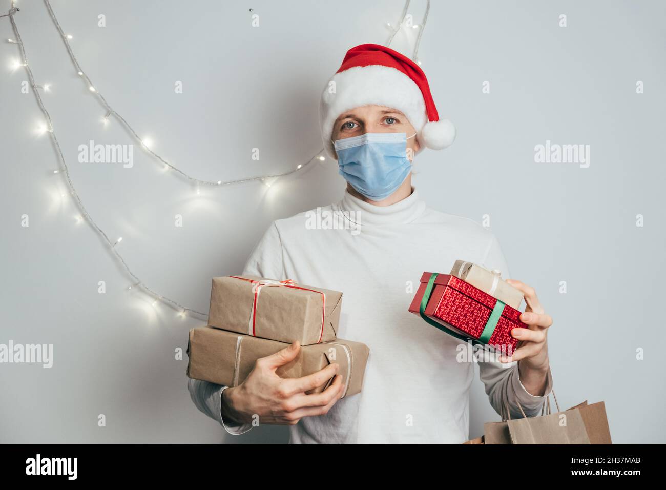 Noël sûr et nouvel an à la maison, homme dans le chapeau rouge de Santa et masque de protection pendant la quarantaine du coronavirus.Pile de cadeaux entre les mains Banque D'Images