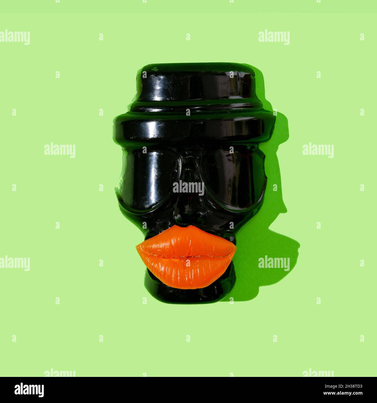 Un crâne noir portant un chapeau et avec des lèvres orange vives sur fond vert néon.Halloween Party invitation concept.Un design artistique effrayant pour banne Banque D'Images