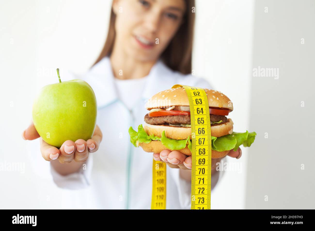 Jeune fille attrayante fait le choix entre la nourriture saine et nocive tenant la pomme et un hamburger dans ses mains. Banque D'Images