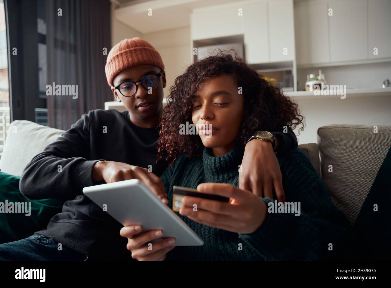 Couple multiethnique achetant des produits en ligne sur une tablette à l'aide d'une carte de crédit, assis sur un canapé dans le salon Banque D'Images