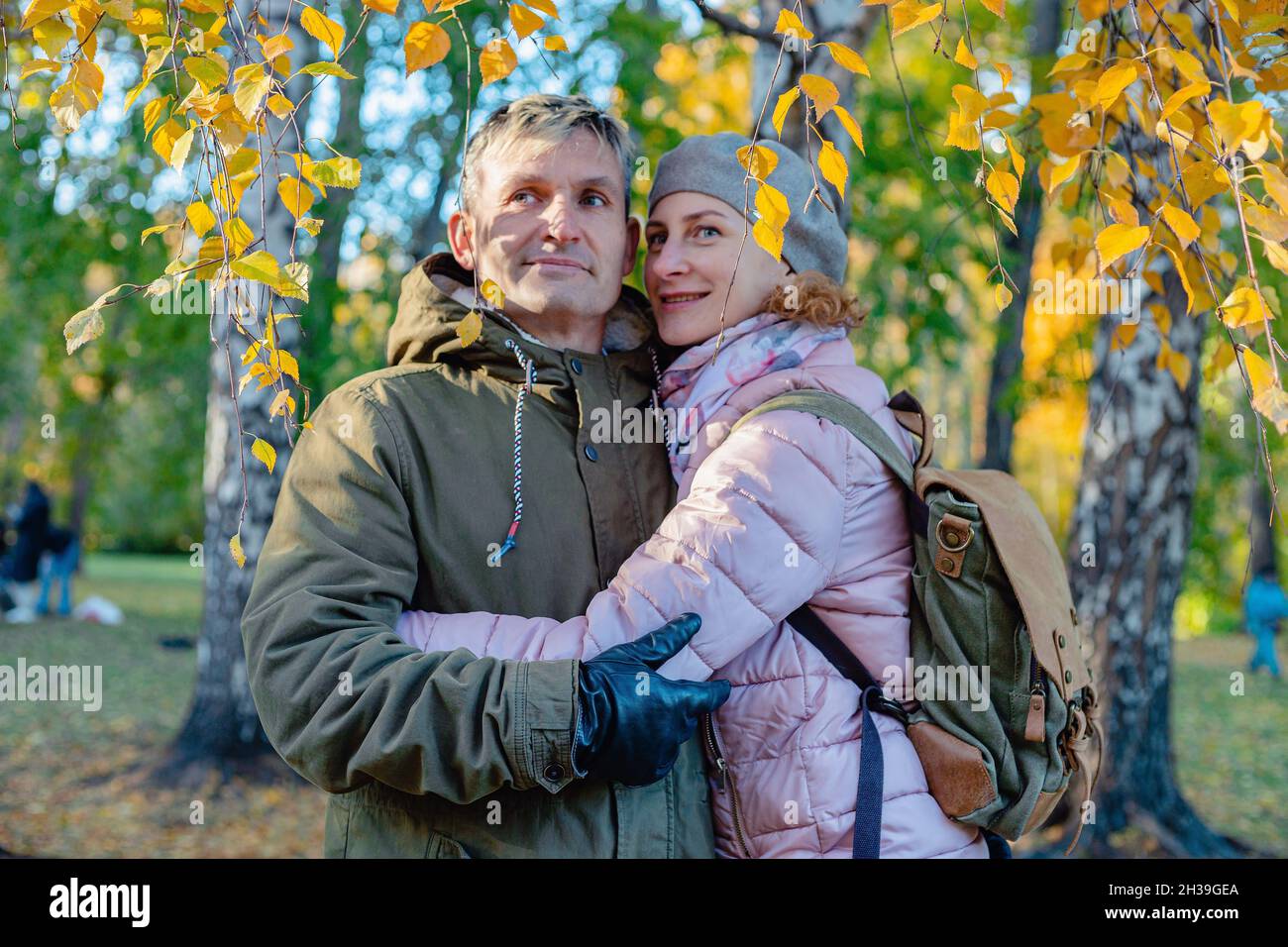 Un couple d'âge moyen souriant à l'extérieur.L'homme et la femme attirants d'origine caucasienne se tiennent à l'embrasser.Arrière-plan du parc d'automne.Jour d'automne ensoleillé. Banque D'Images
