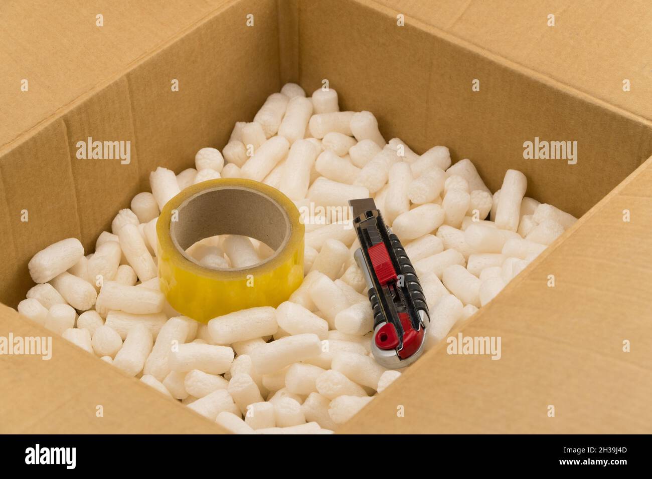 Boîte en carton avec mastic de mousse de polystyrène pour un emballage sûr.Couteau de papeterie et ruban à l'intérieur Banque D'Images