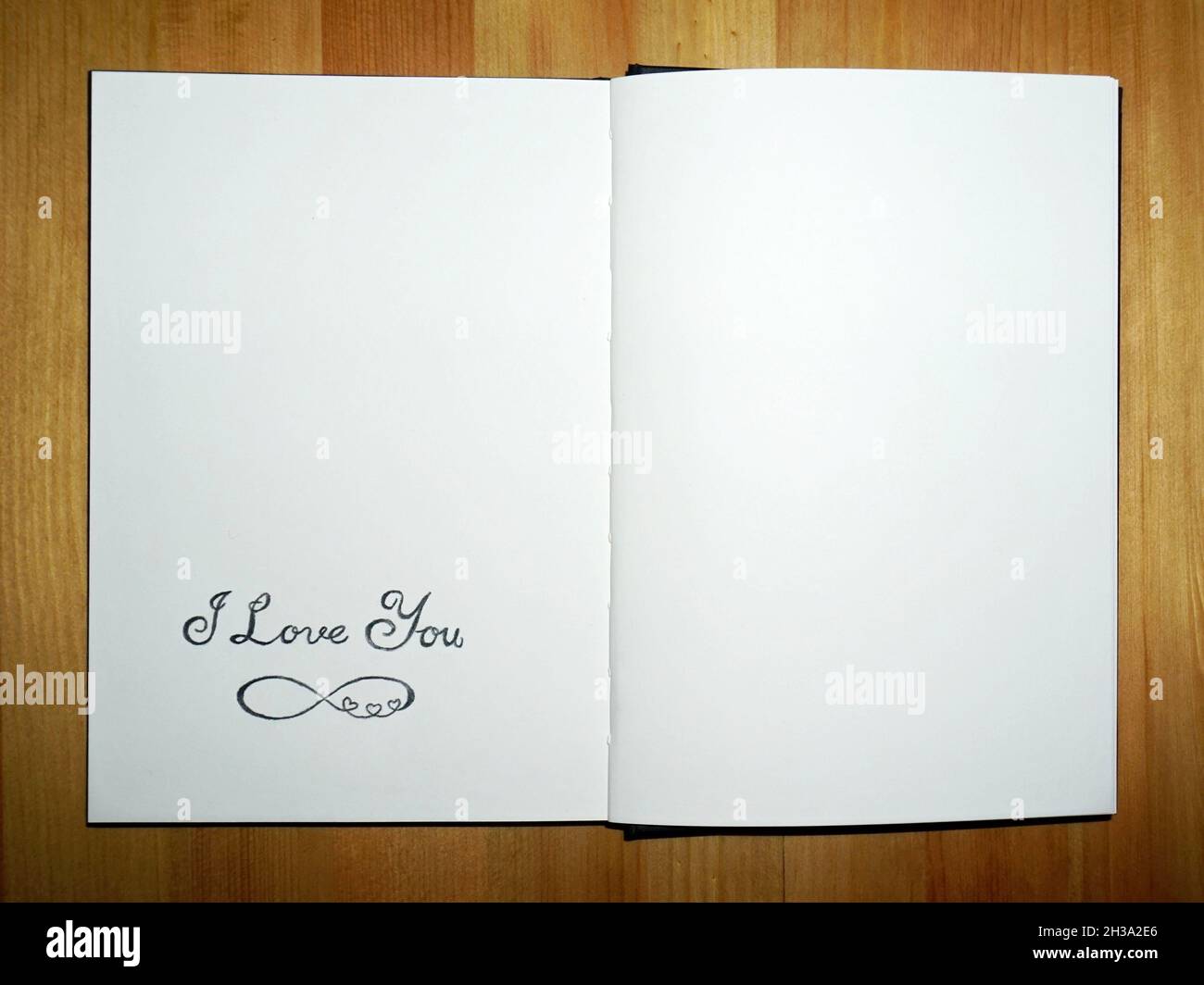Un carnet ouvert avec `I Love You' et le symbole éternité écrit au crayon, sur une table en bois Banque D'Images