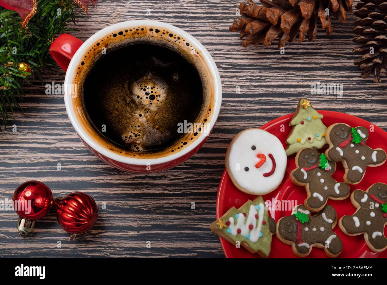 Biscuits enrobés de sucre et biscuits à thème de Noël sur une assiette en céramique rouge avec une tasse de café et décorations de Noël. Banque D'Images