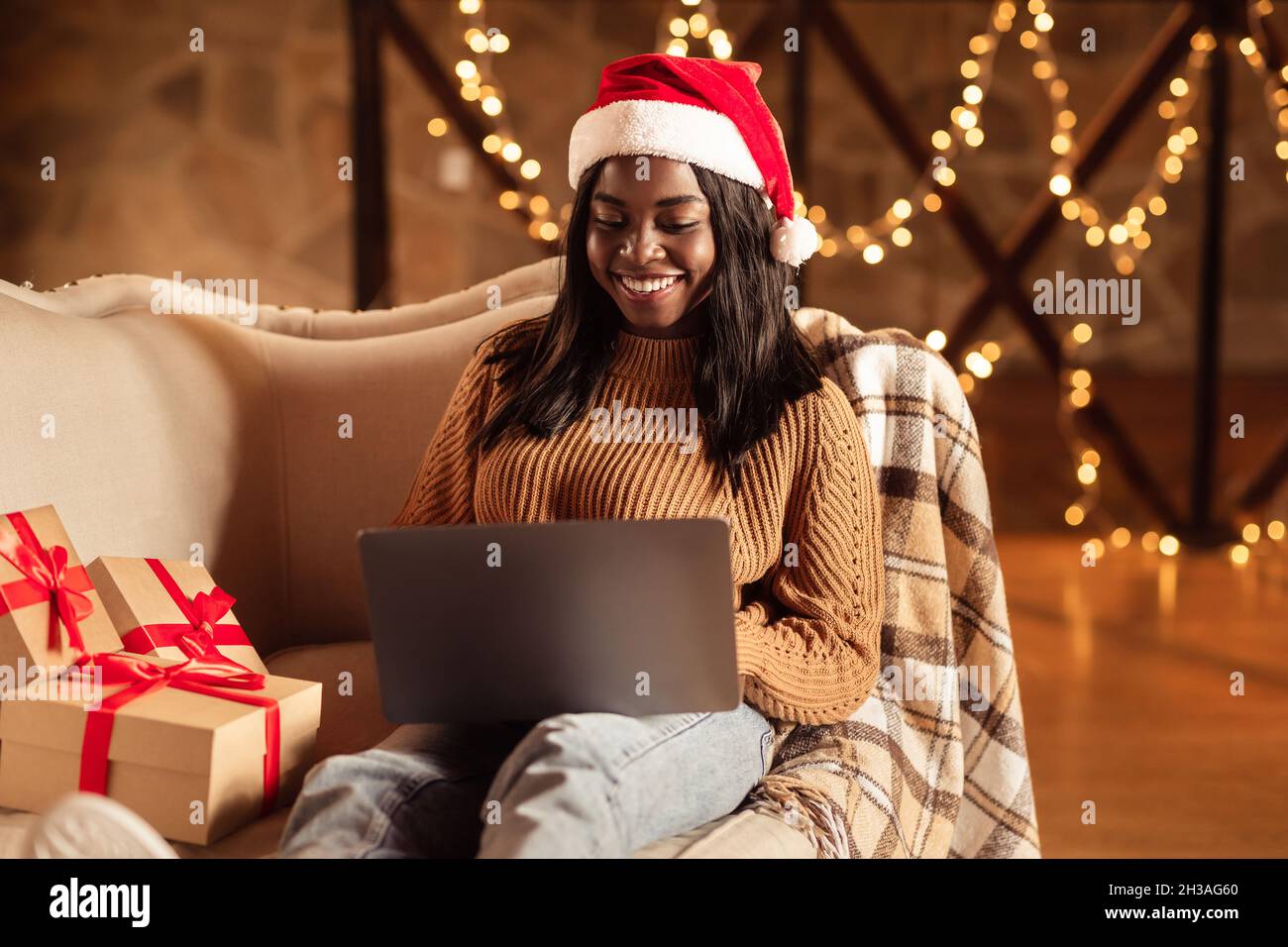 Bonne dame noire dans le chapeau de père Noël en utilisant l'ordinateur  portable, commander des cadeaux de Noël sur le Web, acheter pour des cadeaux  de Noël en ligne à partir de