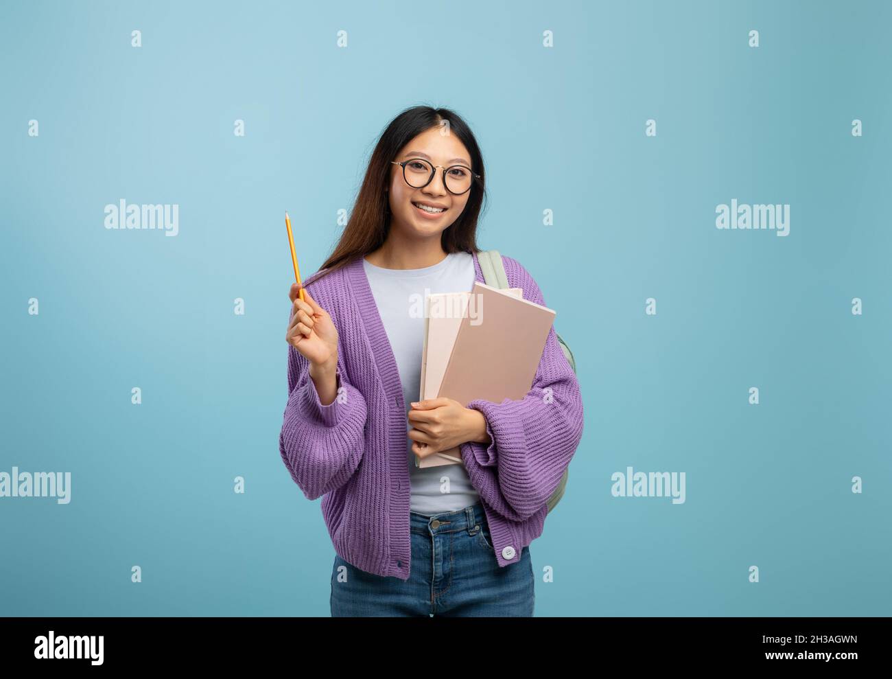 Je connais la réponse.Une étudiante asiatique excitée en lunettes tenant le bloc-notes et le crayon pointant vers le haut, fond bleu Banque D'Images