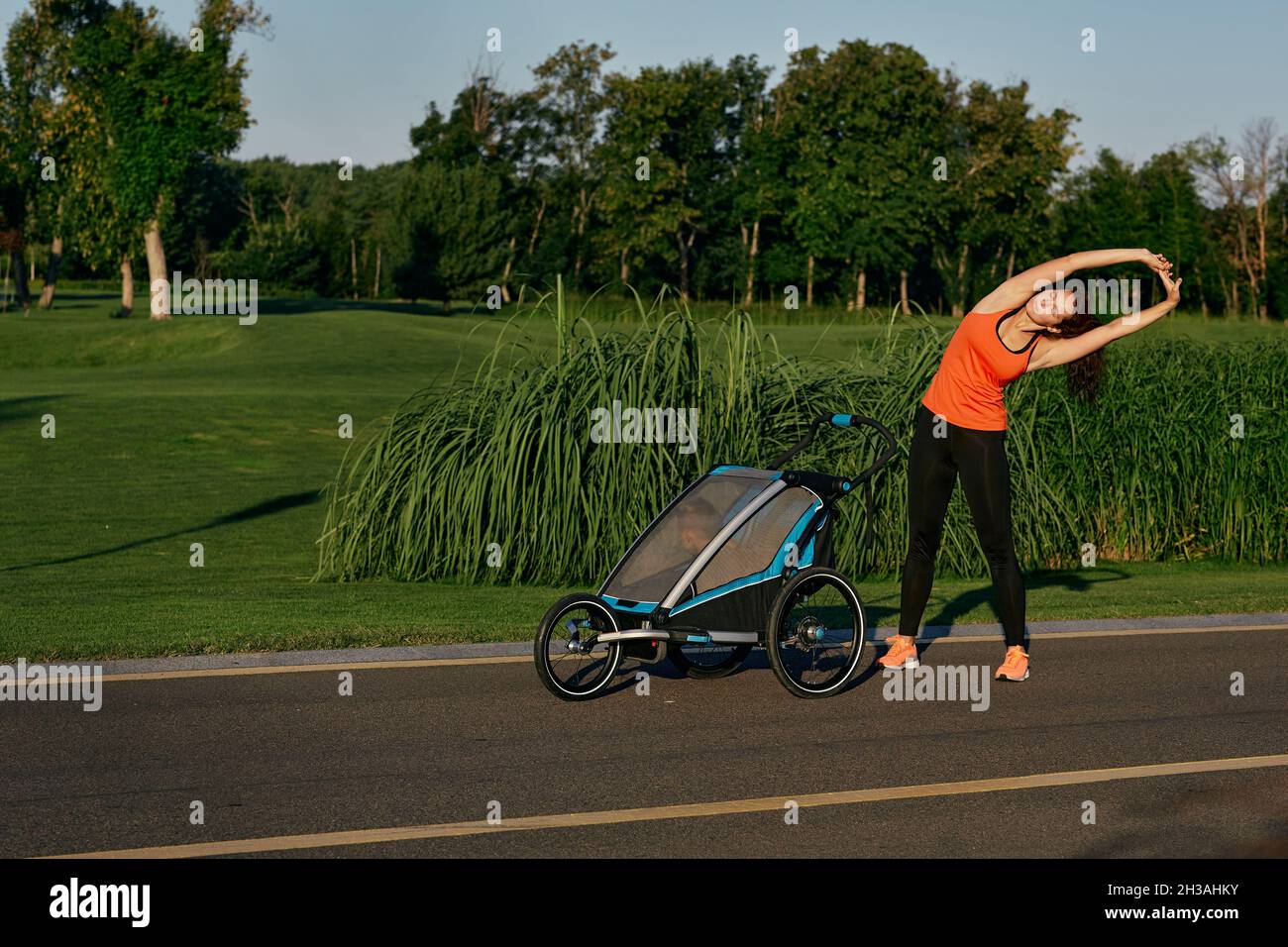 Jeune mère faisant de la gymnastique et de l'exercice en marchant avec son enfant dans la poussette de bébé au parc public de la ville Banque D'Images