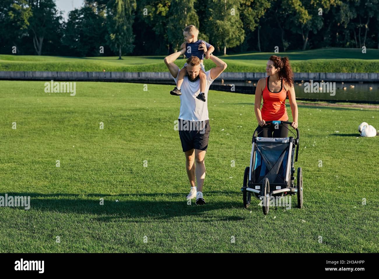 Une jeune famille heureuse avec son enfant passe du temps ensemble tout en marchant avec une poussette sur une pelouse verte dans le parc national.Jour de la famille, parent Banque D'Images
