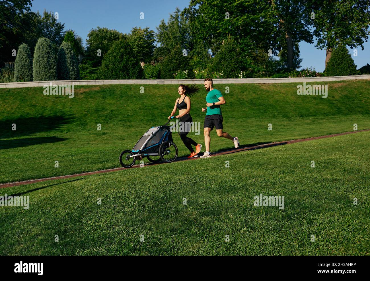 Couple de sports de course poussant poussette de jogging avec enfant dans le parc à l'extérieur.Course matinale pour toute la famille Banque D'Images