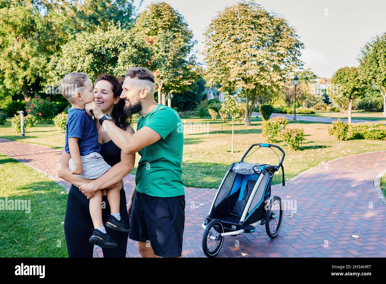 Jour de la famille.Une jeune famille heureuse avec son fils passe un week-end à pied avec une poussette dans le parc vert de la ville Banque D'Images