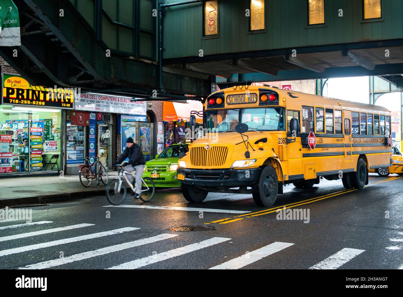 New York, États-Unis. Autobus scolaire jaune traversant la pluie, sur une voie de métro surélevée à Roosevelt Ave, Queens. Banque D'Images