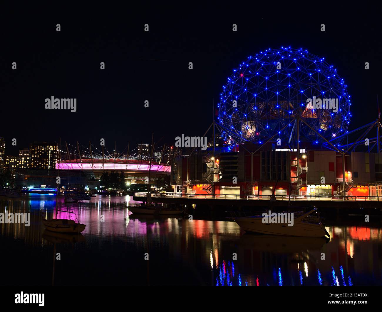 Vue nocturne du Vancouver Science World et du stade BC place avec un horizon illuminé reflété dans l'eau douce de la baie de False Creek. Banque D'Images