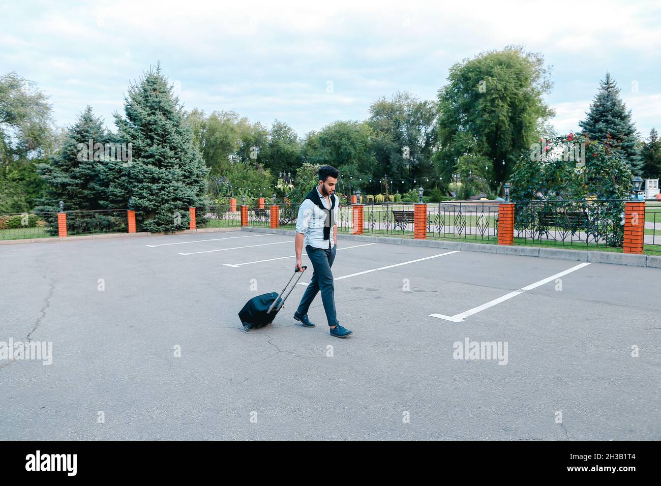 Un jeune beau Guy arabe homme d'affaires Entrepreneur touriste Visiteur aller avec Suitcase pour Voyage dans sa main dans le parking . Banque D'Images