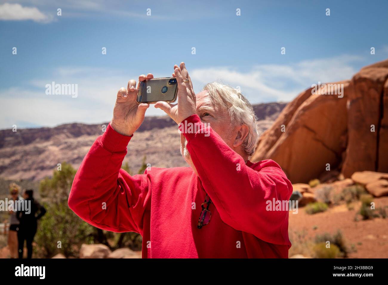 05 23 2021 Arches National Park USA - l'homme senior en chemise rouge prend une photo dans le désert avec un iphone - formation de rocher et d'autres touristes flous Banque D'Images