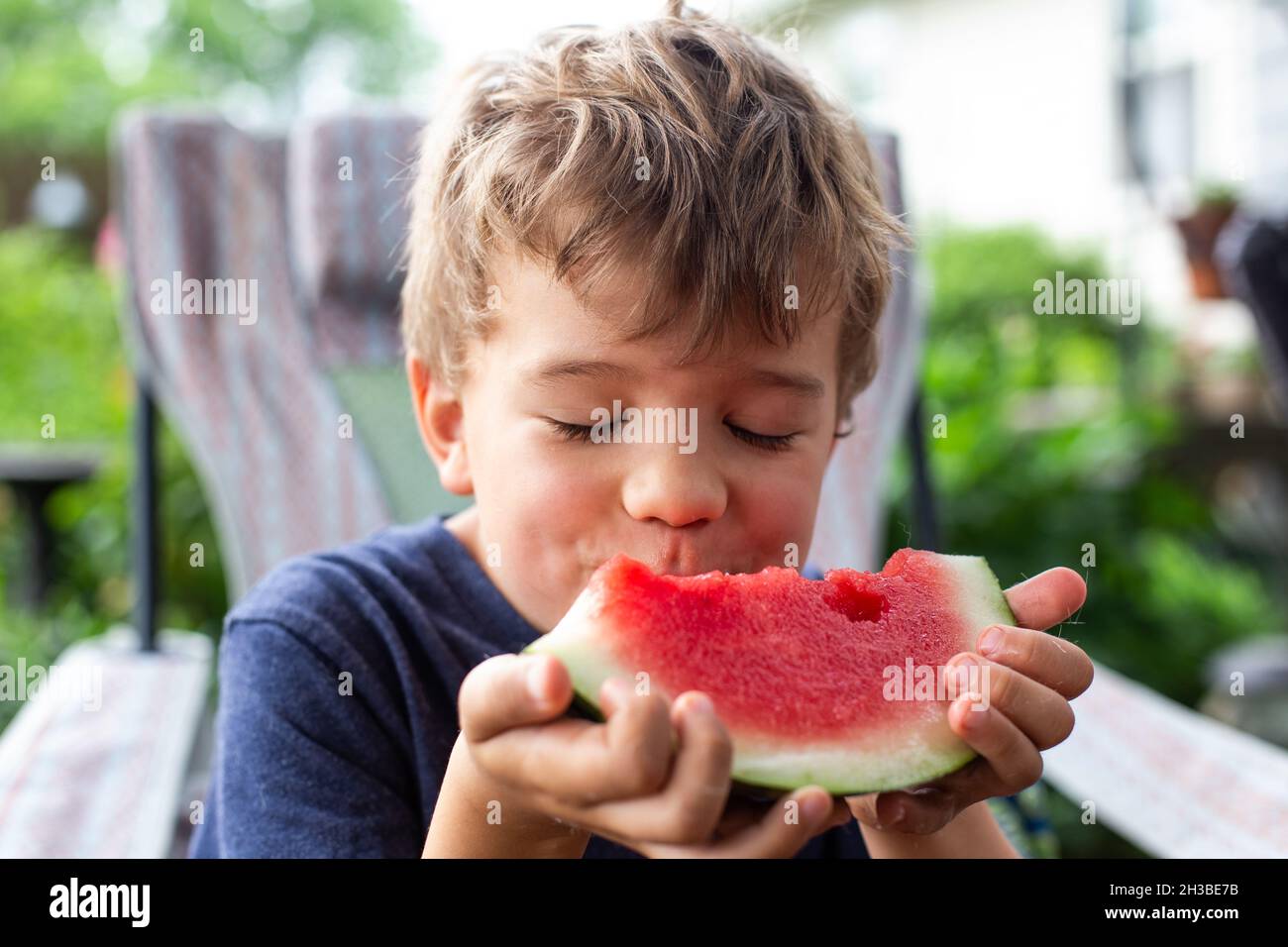 Petit garçon aux cheveux blonds mangeant de la pastèque avec les yeux fermés Banque D'Images