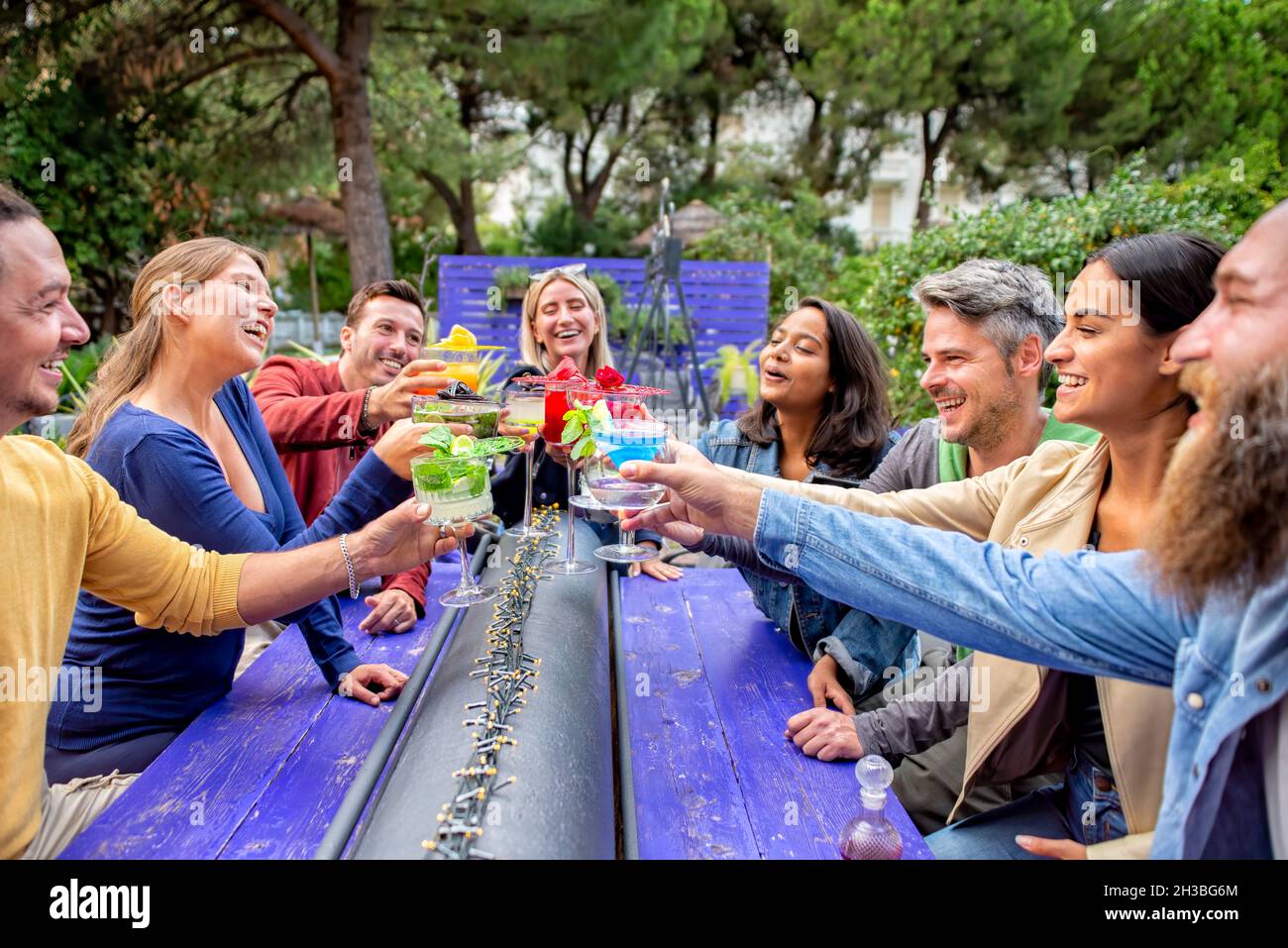 un grand groupe d'amis multiculturels heureux et variés qui font des toasts festifs avec de magnifiques verres à cocktail gastronomiques au bar-restaurant Banque D'Images
