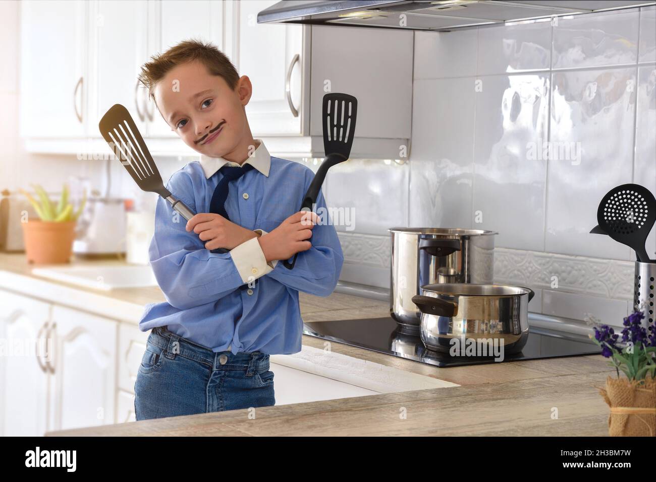 Garçon avec des spatules dans les mains en robe avec chemise et cravate et  la moustache peinte dans une cuisine blanche regardant l'appareil photo  Photo Stock - Alamy