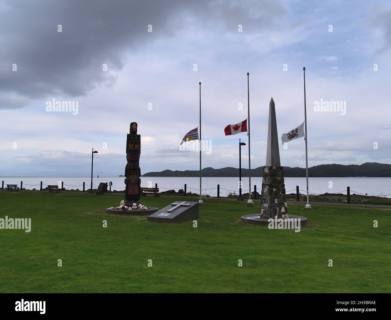 Vue sur le monument commémoratif du parc Carrot, Port Hardy, île de Vancouver avec totem, obélisque et drapeaux sur la côte le jour nuageux de l'automne. Banque D'Images