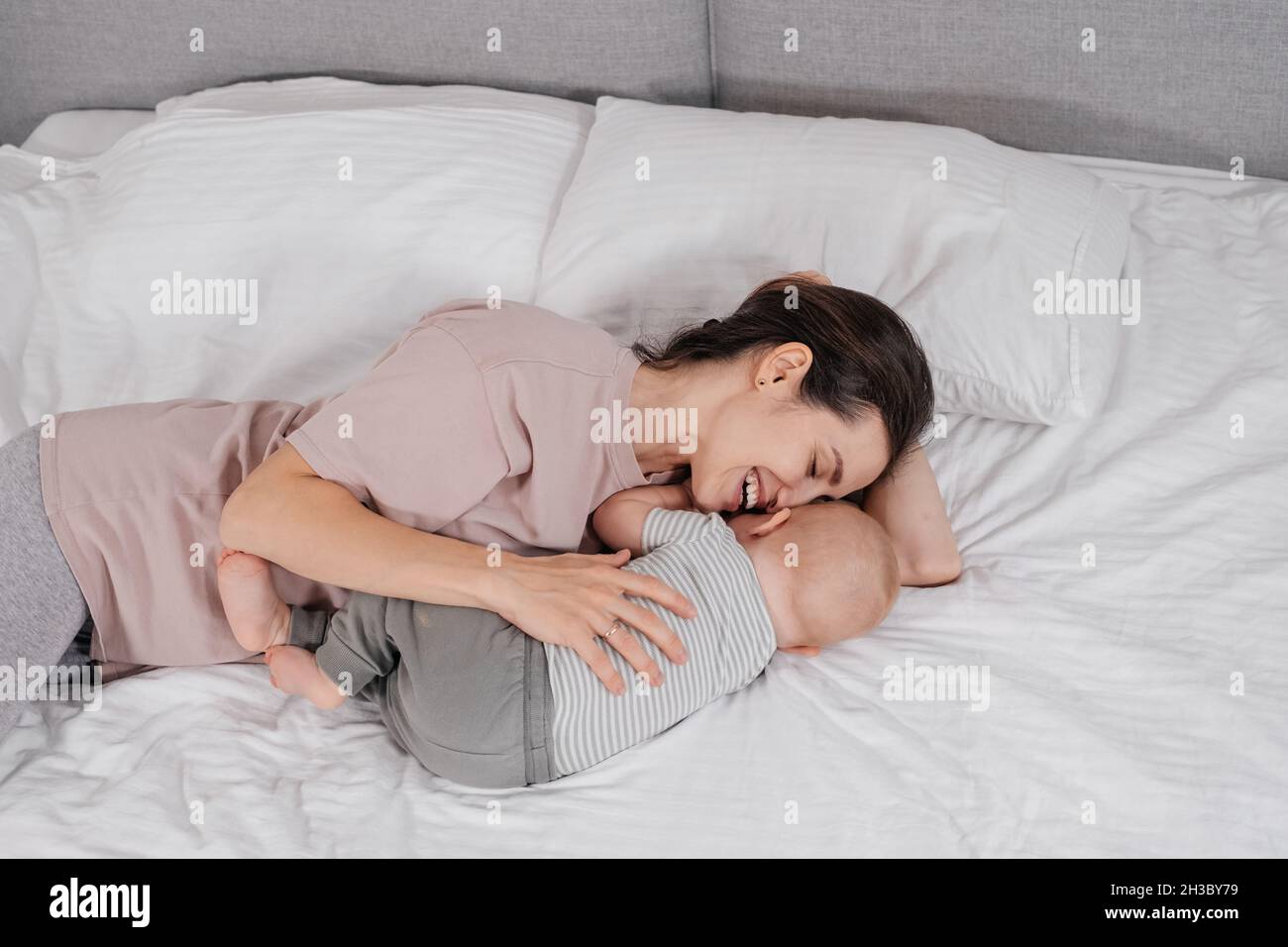 Mère avec bébé garçon en cuddling au lit le matin.Passez un bon moment avec un bébé mignon à la maison, jouant dans une chambre lumineuse après le sommeil. Banque D'Images