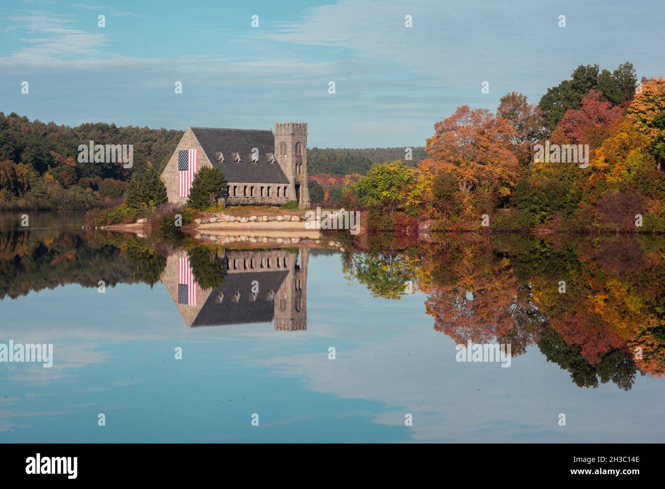 Vieille église en pierre du Massachusetts pendant la saison d'automne avec feuillage d'automne près du lac avec réflexion le jour ensoleillé d'octobre avec drapeau américain Banque D'Images