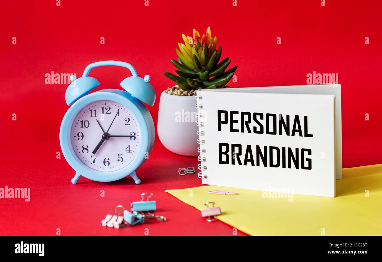 Texte DE MARQUAGE PERSONNEL écrit sur le bloc-notes.Sur un réveil à fond rouge et jaune, cactus et trombones.Projet de conception.Marquage et marketing Banque D'Images