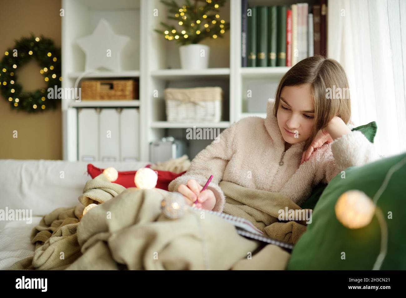 Belle adolescente étudiant ou esquissant accrocheuillé sur le canapé dans un salon confortable à Noël.Enfant mignon passant du temps à la maison pendant le winte Banque D'Images
