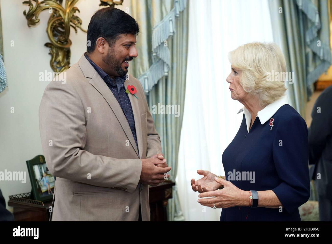 La duchesse de Cornwall s'entretient avec Mirza Shahzad, 36 ans, qui a soutenu l'appel du coquelicot à Bristol, Cardiff, Swansea,Gloucester et Gloucester depuis qu'il a déménagé au Royaume-Uni du Pakistan en 2012, alors que le prince de Galles et la duchesse de Cornwall rencontrent dix collectionneurs de la Royal British Legion (RBL) à Clarence House, Londres, lors du lancement officiel de l'appel de pavot centenaire.Date de la photo: Mardi 26 octobre 2021. Banque D'Images