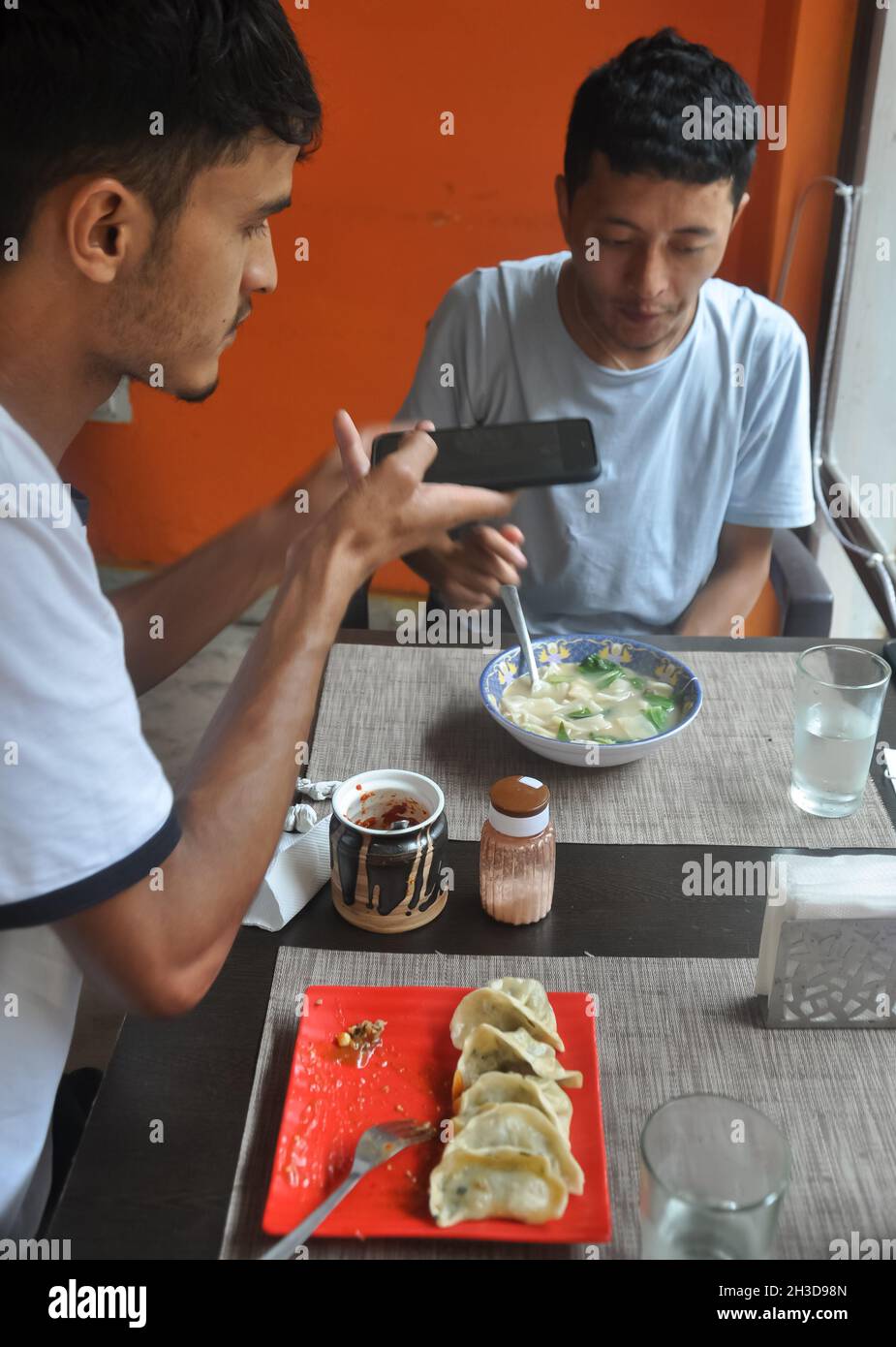 Deux amis de sexe masculin apprécient la restauration rapide au café en prenant des photos de nourriture avec un téléphone portable Banque D'Images