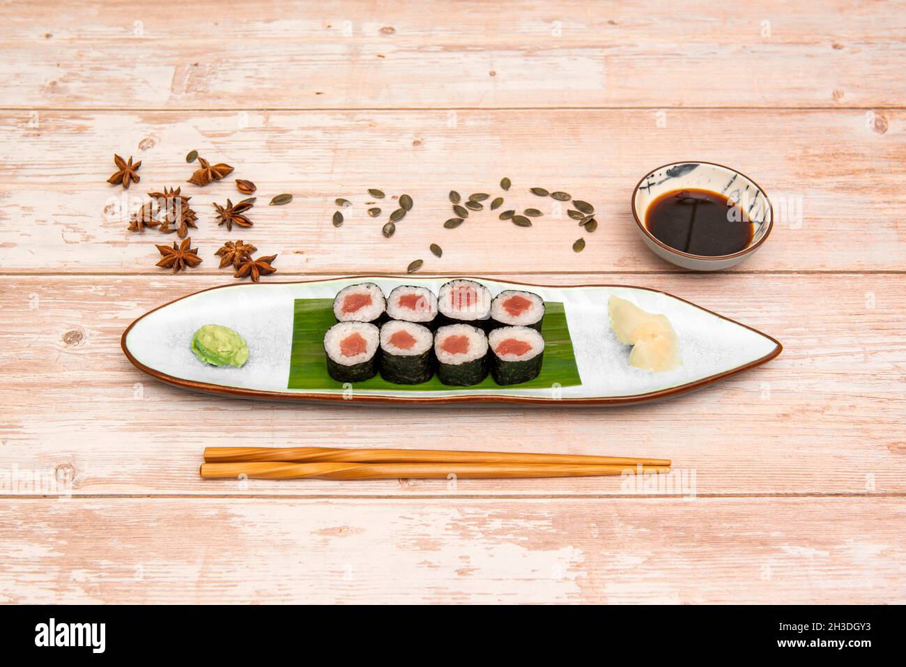 Assiette de maki de thon rouge avec riz blanc et vinaigre japonais avec anis étoilé, graines de citrouille, baguettes et sauce soja sur table en bois Banque D'Images