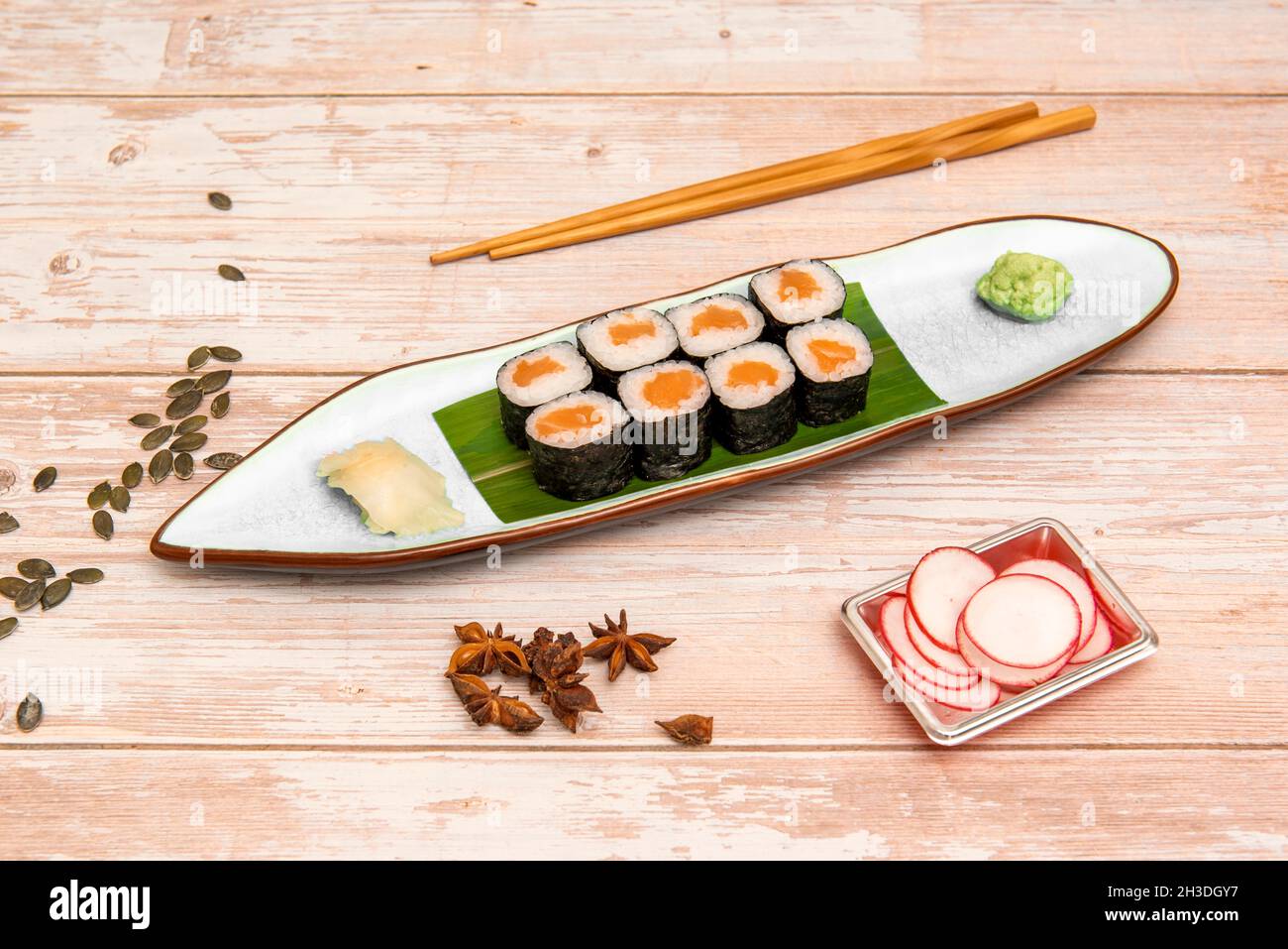 Plat maki au saumon norvégien avec riz blanc, vinaigre japonais avec wasabi, ginseng, baguettes, radis, graines de citrouille et anis étoilé Banque D'Images
