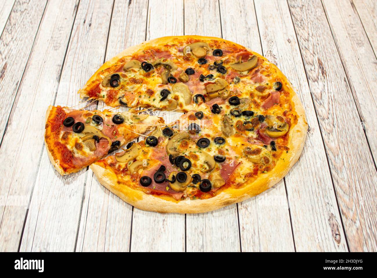Petite pizza à croûte mince avec des tranches d'olives noires, des tranches de champignons, du jambon cuit, de l'origan et une portion qui étire le fromage mozzarella fondu Banque D'Images