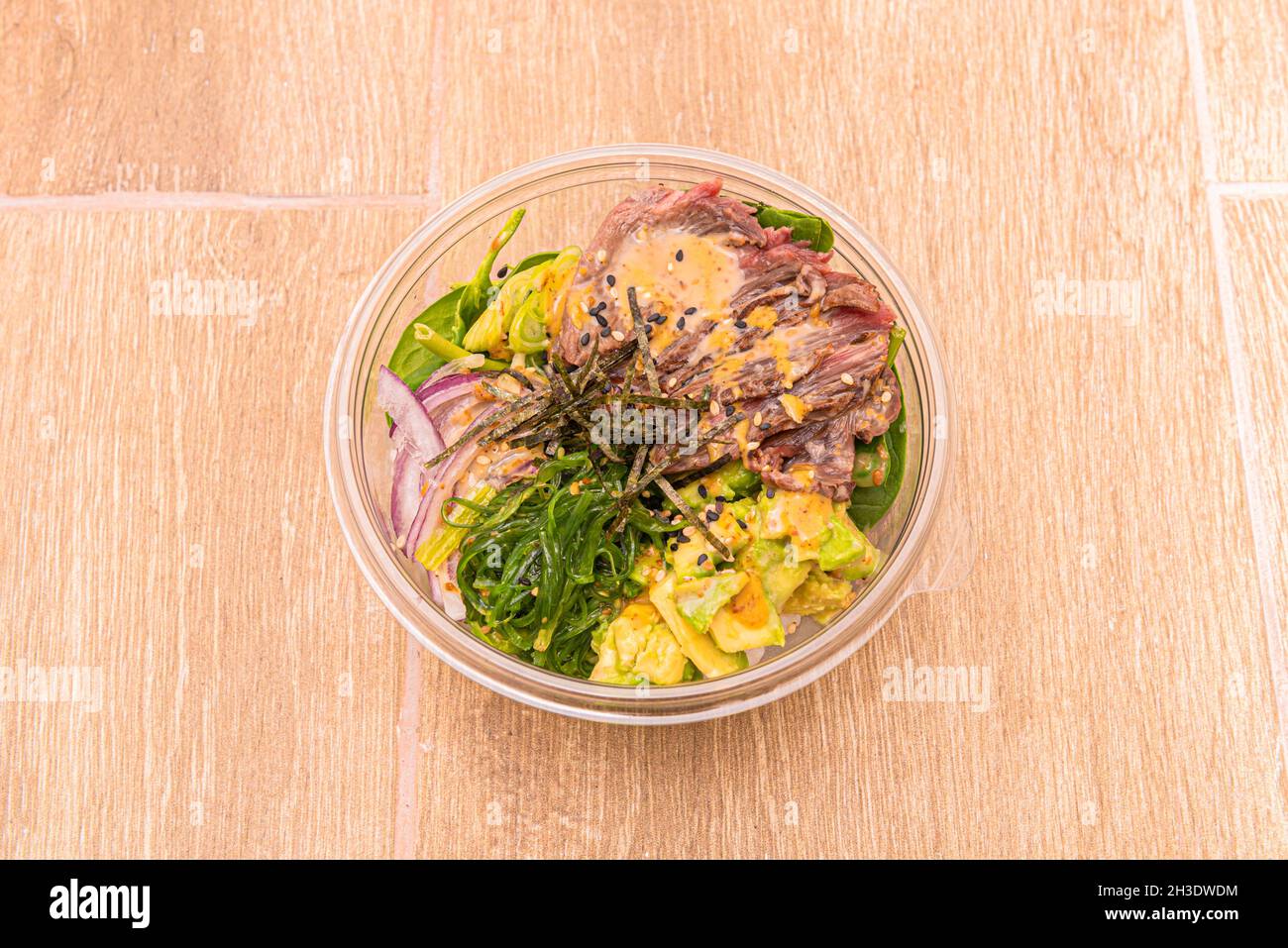 Poke Bowl dans un récipient à emporter en plastique avec oignon rouge, algues wakame, bœuf, avocat mûr et épinards Banque D'Images