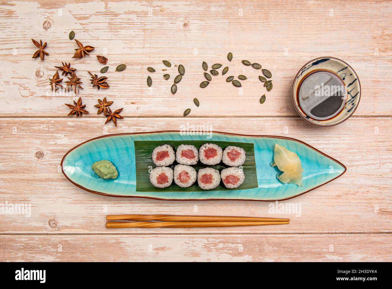 Service de maki de saumon rouge japonais roulé avec du riz et de l'algue nori présenté sur un plateau bleu avec des baguettes en bois, l'anis étoilé, les graines de citrouille et s Banque D'Images