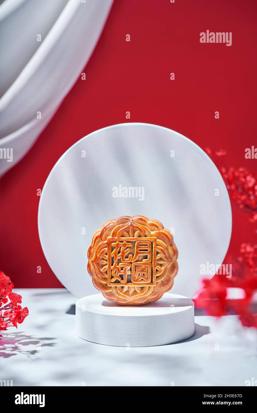 Gâteau de lune traditionnel chinois sucré cuit rond servi sur une table avec des fleurs sur fond rouge dans un studio lumineux moderne Banque D'Images