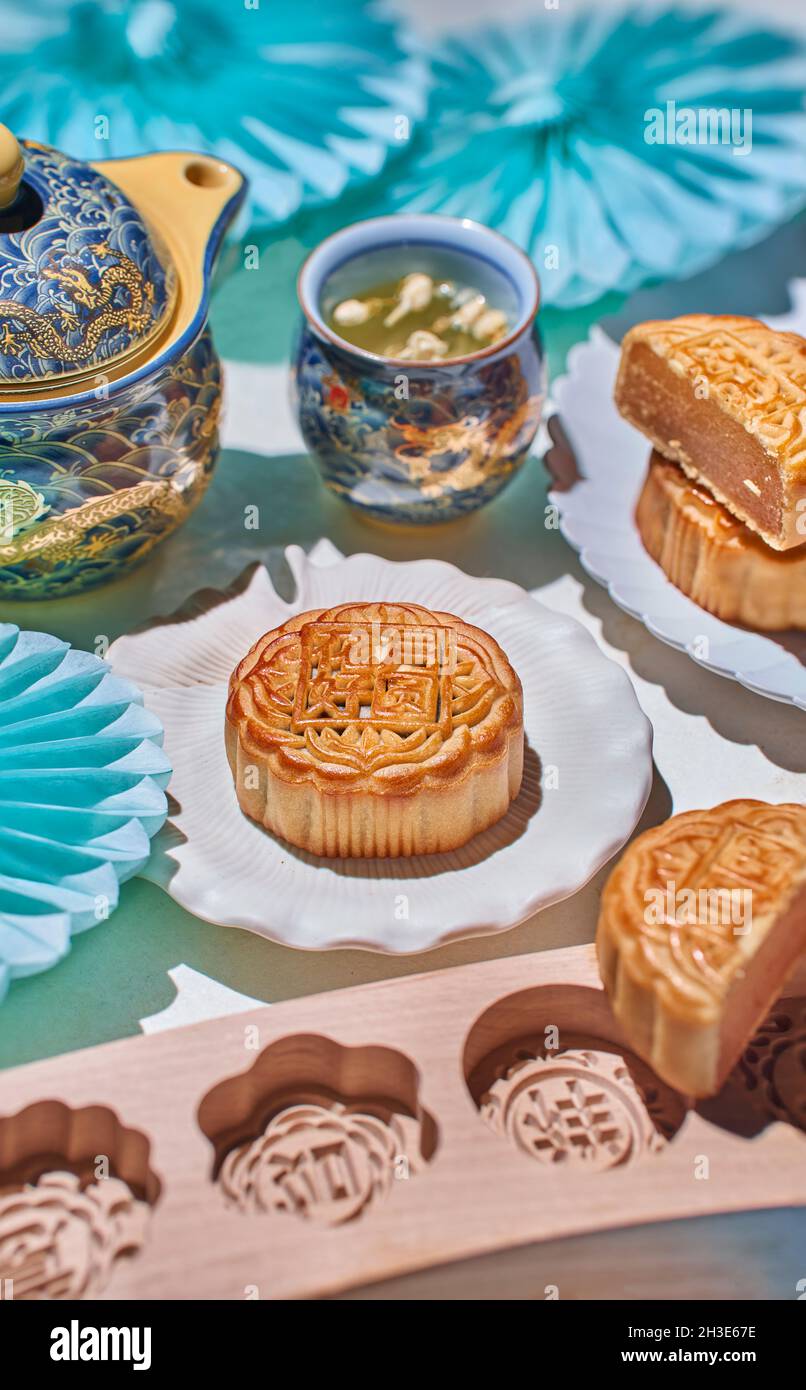 Des gâteaux de lune traditionnels avec garniture servis sur une table avec des moules à pâtisserie près de la bouilloire avec du thé aux herbes dans une pièce lumineuse Banque D'Images
